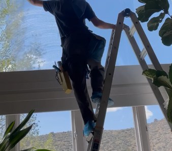 Technician on a ladder cleaning tall interior windows