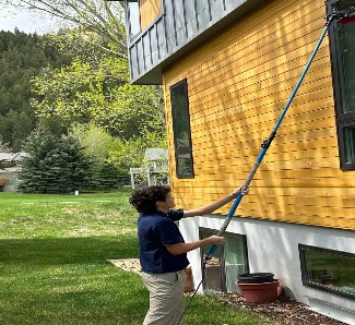 Technician cleaning windows on a yellow-sided home
