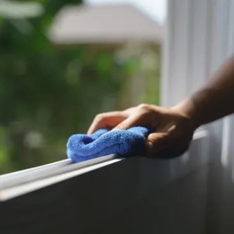 Hand wiping a window sill with a microfiber cloth
